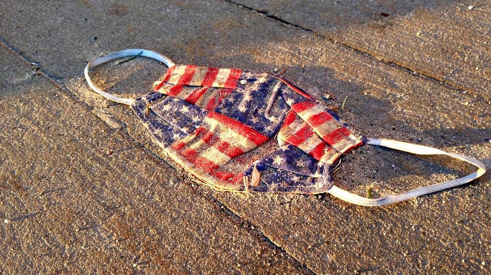 An American flag mask dropped on the ground and dirty.